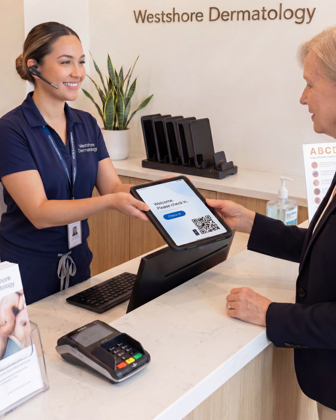 A dermatology front-desk staffer hands a patient an iPad in a CONNECT case at the reception counter, with a MultiDock charging several iPads in the background